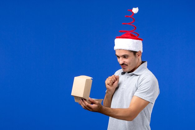 Front view young male holding food package on blue wall male food service job