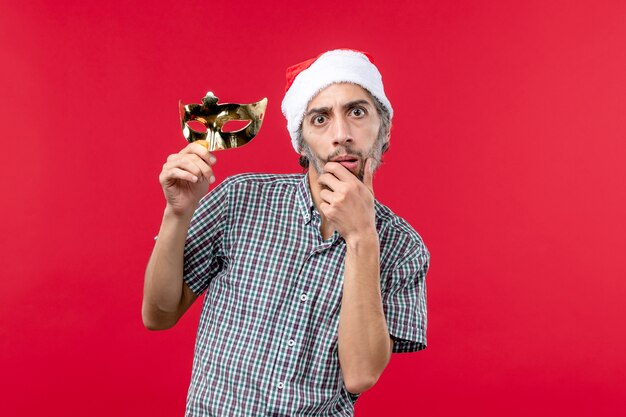 Front view of young male holding golden mask on red