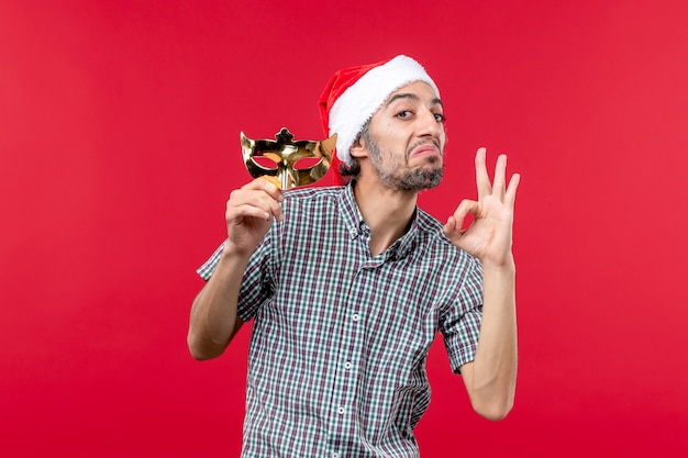 Front view of young male holding golden mask on red