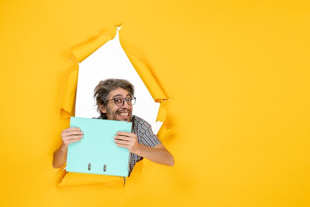 Front view of young male holding green file on yellow wall