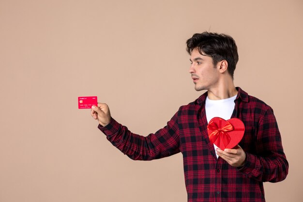 갈색 벽에 하트 모양의 선물과 은행 카드를 들고 있는 전면 보기 젊은 남성