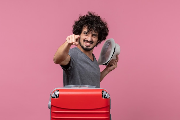 Free photo front view young male holding his hat and preparing for vacation on light pink space