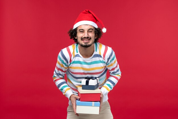 Front view young male holding holiday present on red wall holiday new year emotion