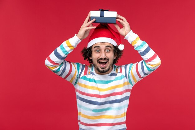 Front view young male holding holiday present on red wall new year holiday emotion