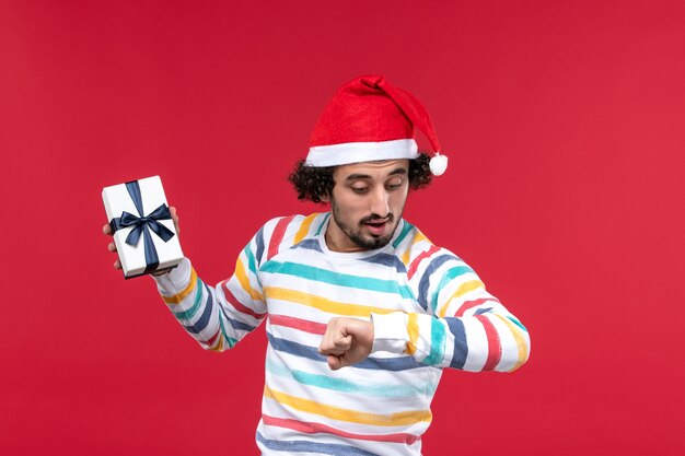 Front view young male holding holiday present on red wall new year holidays emotions