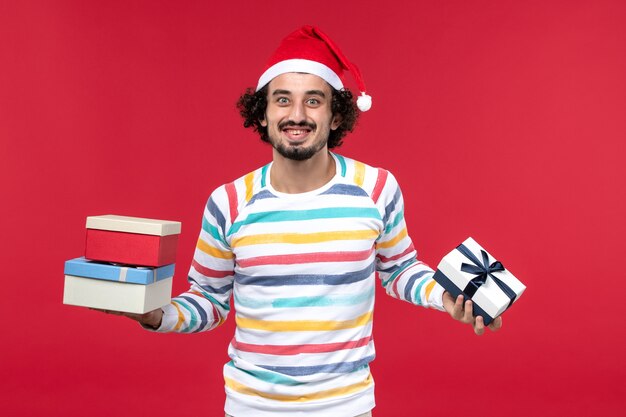 Вид спереди молодой мужчина держит праздничные подарки на красном полу новогодние эмоции красный