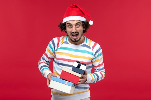 Free photo front view young male holding holiday presents on red wall holiday new year emotion