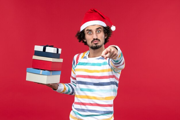 Front view young male holding holiday presents on red wall holiday new year emotions