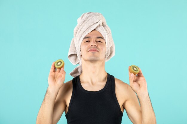 front view young male holding kiwi slices against pimples on his face on a blue background