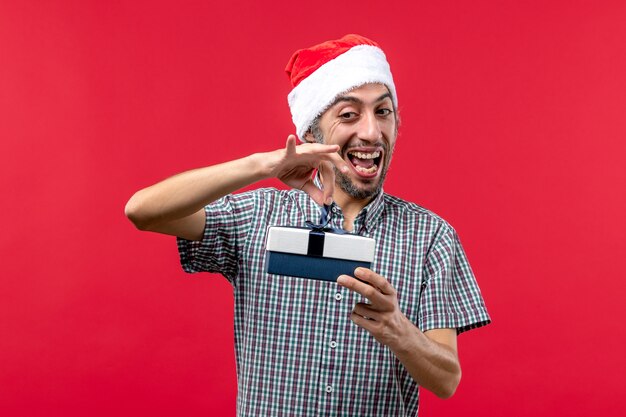Вид спереди молодого мужчины, держащего маленький рождественский подарок на красном