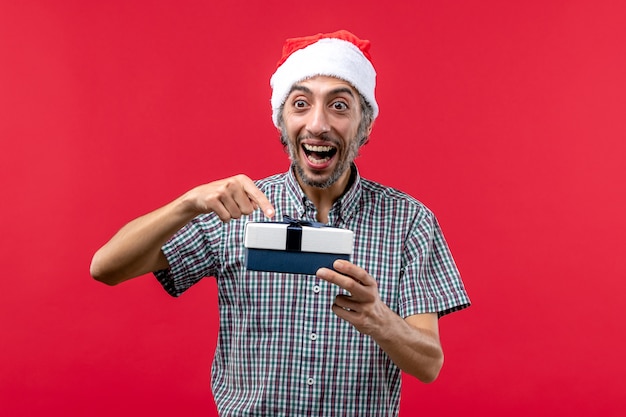 Front view of young male holding little christmas present on red