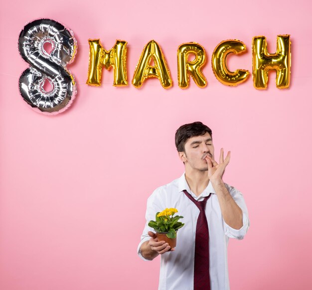 Front view young male holding little flower in pot with march decoration on pink background color present man equality womens day party feminine marriage