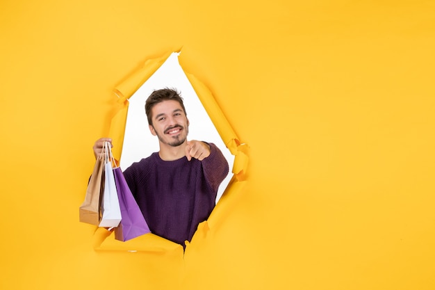 Front view young male holding little packages after shopping on yellow background present xmas color holiday gift