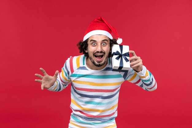 Front view young male holding little present on red background red emotions holiday new year