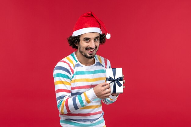 Front view young male holding little present on red wall emotions holidays new year red