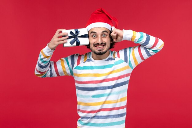 Front view young male holding little present on red wall holidays new year emotions red