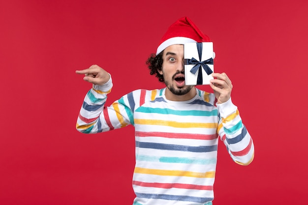 Free photo front view young male holding little present on red wall new year holiday emotions red