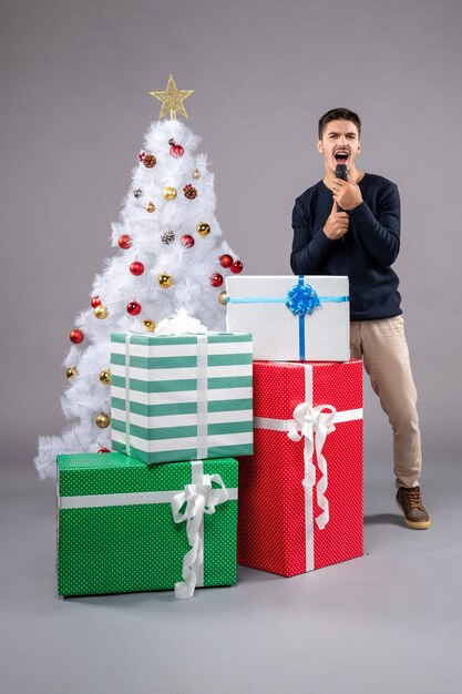 Front view young male holding mic with presents on a grey