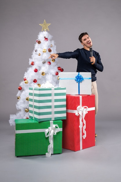 Front view young male holding mic with presents on grey