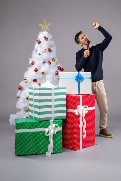Front view young male holding mic with presents on the grey