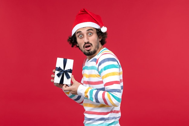 Front view young male holding new year present on a red background holiday new year emotion