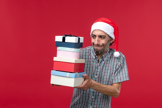 Front view young male holding new year presents on red desk