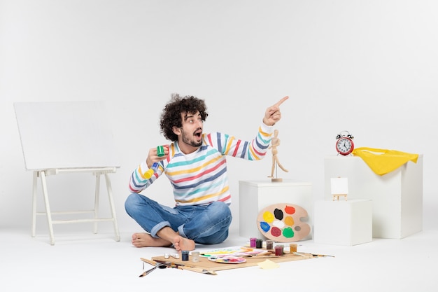 Front view of young male holding paints for drawing inside little cans on white wall