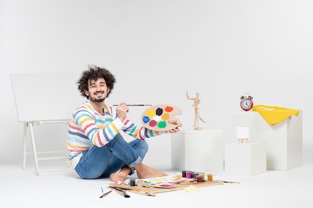 Front view of young male holding paints and tassel for drawing on a white wall