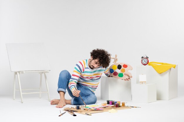 흰 벽에 그림을 그리기 위해 페인트와 술을 들고 있는 젊은 남성의 전면 모습