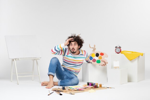 Front view of young male holding paints and tassel for drawing on white wall