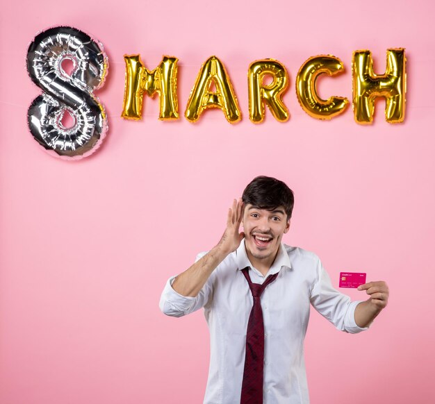 Front view young male holding pink bank card with march decoration on pink background color money party present holiday equality shopping man