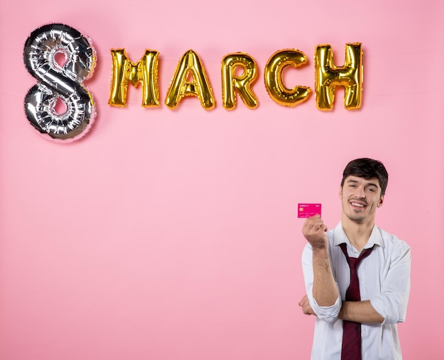 Front view young male holding pink bank card with march decoration on pink background feminine equality colors money holiday shopping man present party