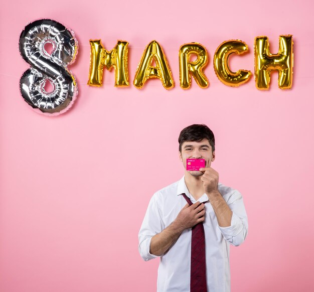 Front view young male holding pink bank card with march decoration on pink background man feminine color party shopping money equality holiday