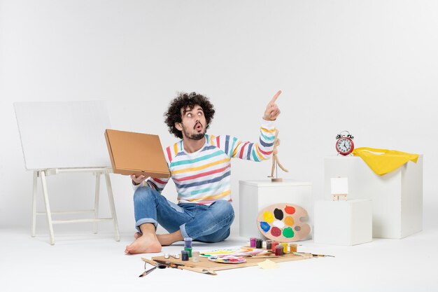 Front view of young male holding pizza box on a white wall