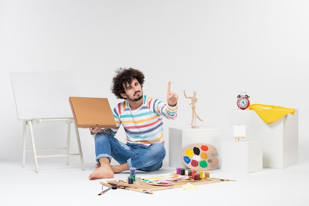 Front view of young male holding pizza box on white wall