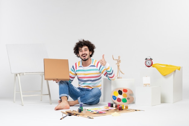 Front view of young male holding pizza box on white wall