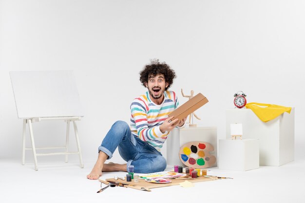 Front view of young male holding pizza box on white wall