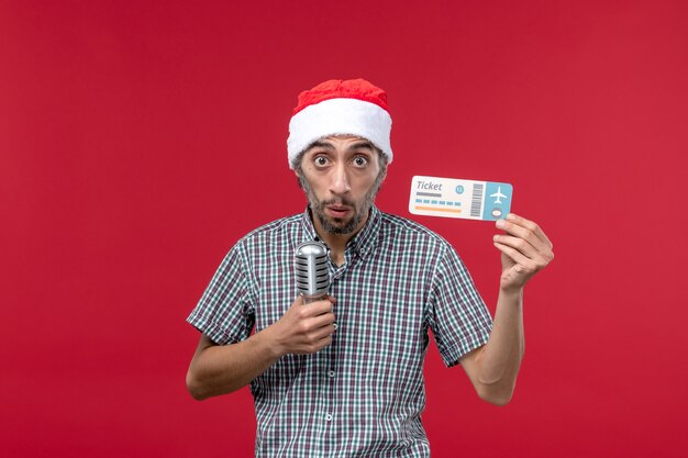 Front view young male holding plane ticket and mic on red background