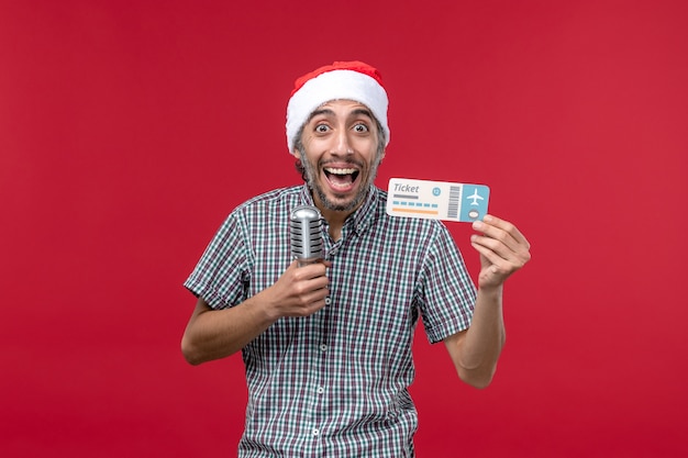 Front view young male holding plane ticket and mic on red background