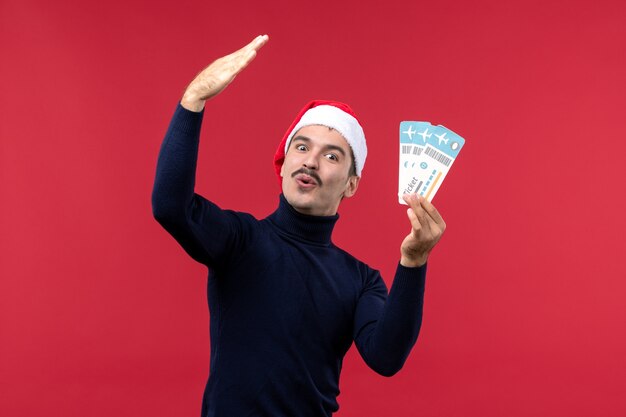 Front view young male holding plane tickets on the red background