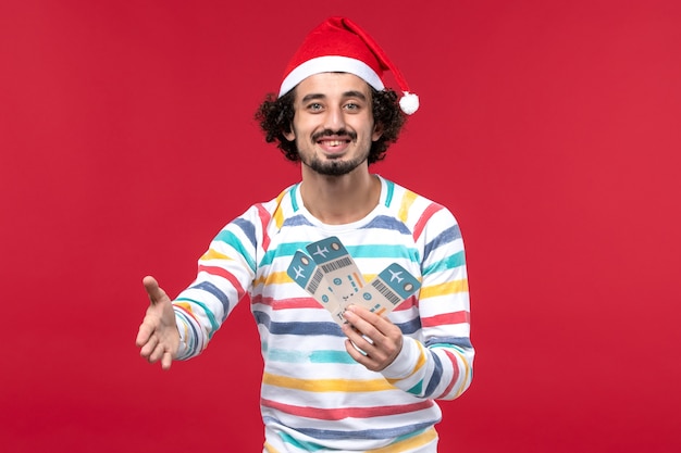 Free photo front view young male holding plane tickets on red floor red holiday new year plane