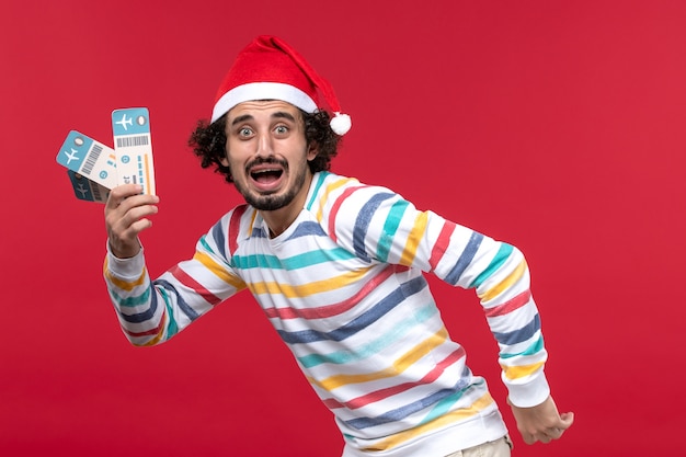 Front view young male holding plane tickets on the red wall plane holidays new year red