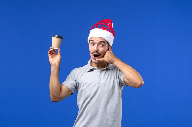 Вид спереди молодой мужчина держит пластиковую кофейную чашку на синей стене мужской новогодний праздник