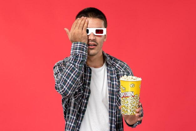 Вид спереди молодой мужчина держит попкорн в солнцезащитных очках -d на красной стене мужской кинотеатр кино фильм