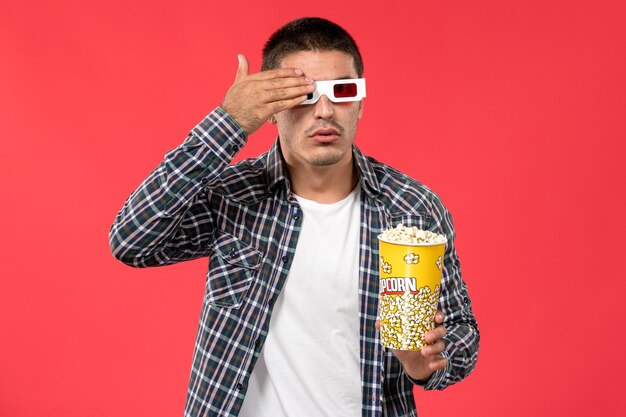 Front view young male holding popcorn package in -d sunglasses on light-red wall cinema movie theater film male