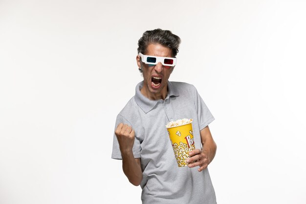 Front view young male holding popcorn package in d sunglasses and rejoicing on white surface