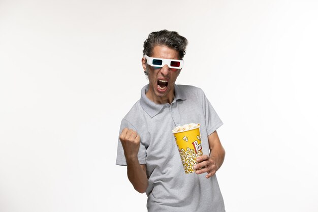 Вид спереди молодой мужчина держит пакет попкорна в солнцезащитных очках d и радуется на белой поверхности