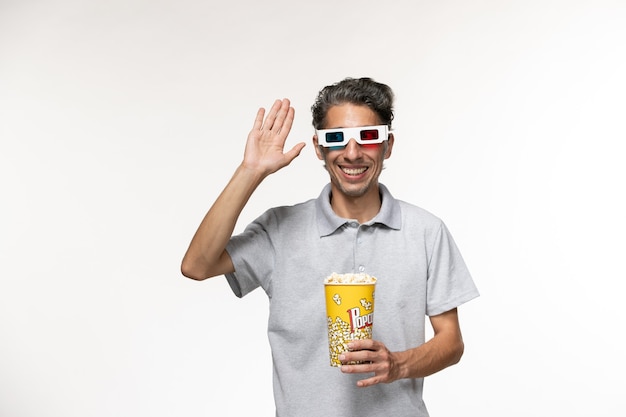 Front view young male holding popcorn package in d sunglasses smiling on a white surface