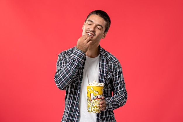 Вид спереди молодой мужчина держит пакет попкорна, ест на светло-красной стене кинотеатр фильм фильм