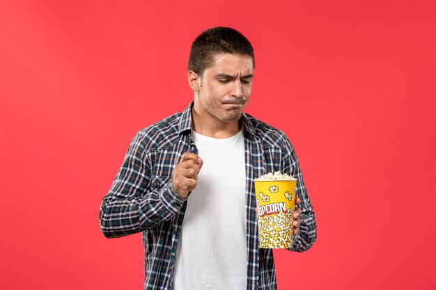 Front view young male holding popcorn package on light red wall cinema theater film movie